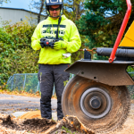 Professional worker operating a stump grinder to remove a tree stump and clear wood debris.